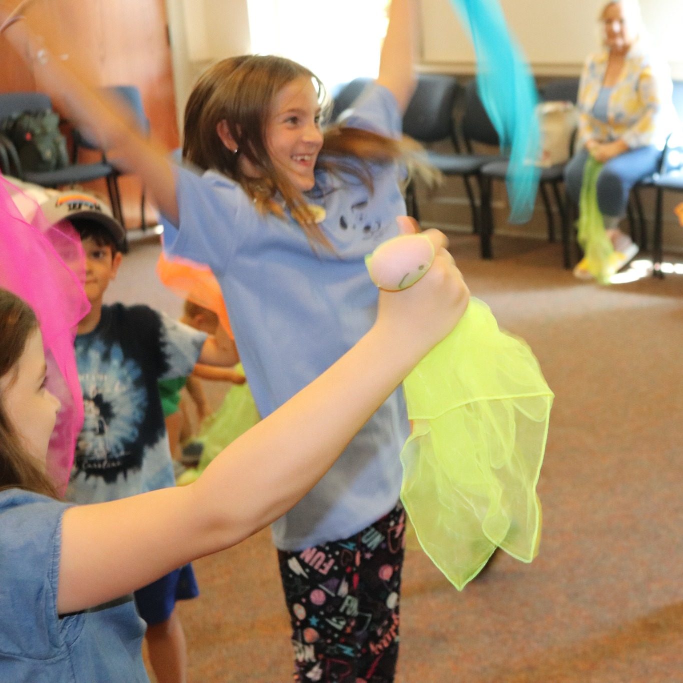 Children dancing and celebrating with musical instruments and scarves. 
